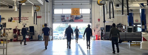 Cohort of 6 people in an automotive shop walking towards an open garage door